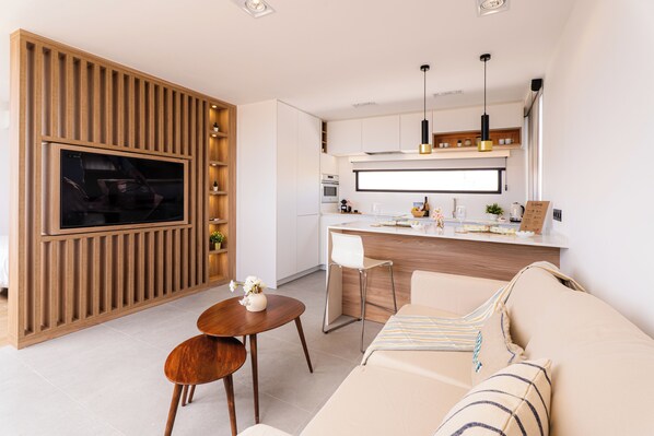 Une cuisine moderne dotée d’un téléviseur encastré, un coin repas avec une table et des chaises, et un salon avec un canapé et une table basse.