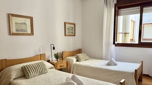 Ett hotellrum med två sängar, ett nattduksbord, en lampa och två inramade tavlor på väggen.