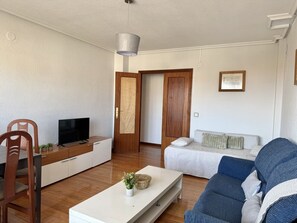 Ein Wohnzimmer mit Fernseher, einer Couch und einem Essbereich mit Stühlen.