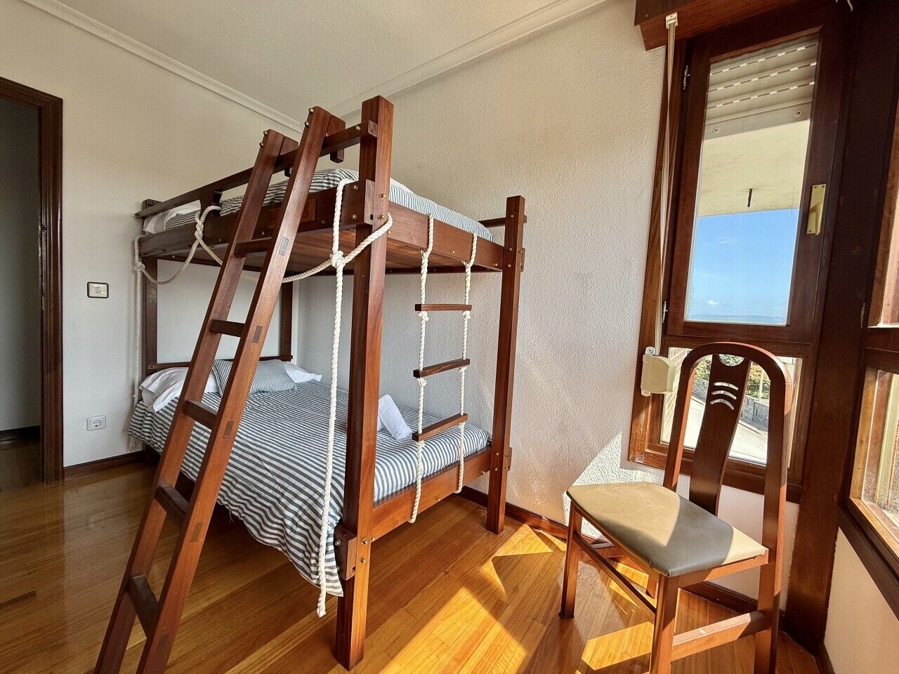 Una cama litera con escalera, una silla y una ventana con vistas.