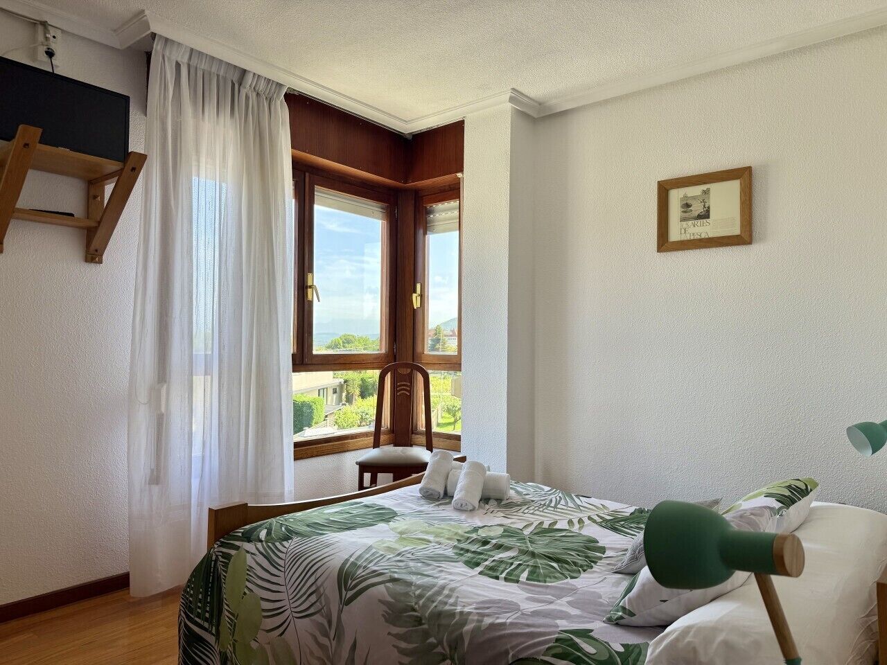 A bedroom with a bed, a chair, a desk, a window with curtains, and a framed picture on the wall.