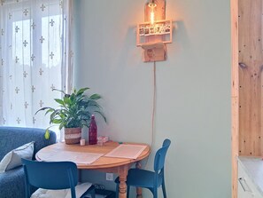 Ein gemütlicher Essbereich mit Holztisch, blauen Stühlen, einer Topfpflanze und einer Wandleuchte.