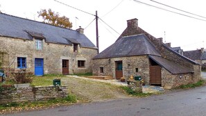 A stone building with a steeply pitched roof and a small porch. - Gîte Youna - stone charm & secret garden (Lizio)