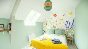 Een slaapkamer met een schuine kap, een dakraam, een bed met een gele sprei, een radiator en een wand met bloemenbehang.