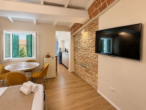 A compact hotel room with a dining area, a TV mounted on the wall, a small kitchen, and a view through a window with shutters. - Pitti Suite 1 (Florence)