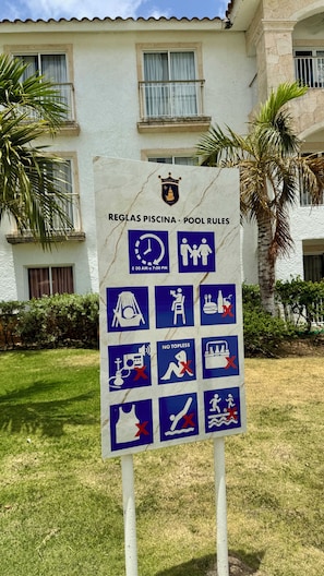 A sign with pool rules in front of a building with a white facade and balconies.