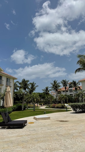 A resort courtyard with palm trees, a lounge chair, and a building with a tiled roof.