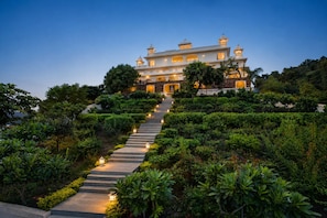 A large, multi-story building with a grand entrance, surrounded by well-maintained gardens and a stone staircase leading up to it.