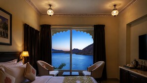 Ein Hotelzimmer mit Bett, zwei Stühlen, einem Fernseher, einer Lampe und Blick auf ein Gewässer.