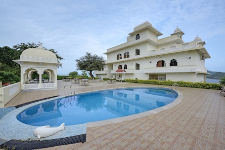 A large building with a swimming pool, a gazebo, and a view of the mountains.. The Karni Mahal-Jaisamand Island Resort
