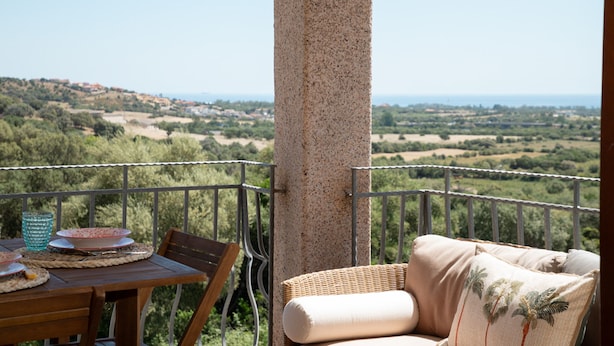 A balcony with a table set for dining, a wicker chair, and a view of a hilly landscape. - Casa Luna e Sole by Wonderful Italy (Budoni)