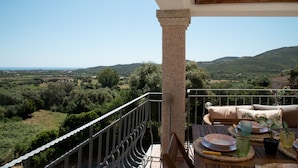 A balcony with a view of a hilly landscape, a table set with plates and glasses, and a cushion on a chair. - Casa Luna e Sole by Wonderful Italy (Budoni)