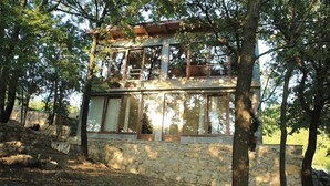 Ein Steinhaus mit mehreren Fenstern und einem Balkon, umgeben von Bäumen.