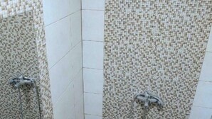 Ein Badezimmer mit gefliesten Duschwänden, einem Waschbecken inklusive Spiegel und einer Duschbrause.