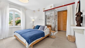 Un dormitorio con cama, ventana, mesita de noche, lámpara, armario de madera y espejo.