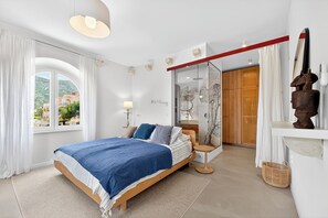 Ein Schlafzimmer mit Bett, Fenster, Nachttisch, Lampe, Holzschrank und Spiegel.