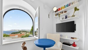 Een kamer met een ronde blauwe tafel, een witte stoel, een boekenplank en een televisie aan de muur.