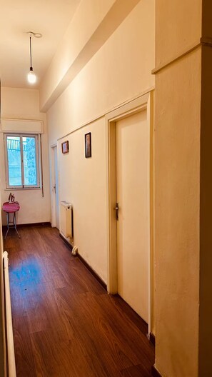 A hallway with wooden flooring, a radiator, a door, and a window with a view of trees. - Spacious 6-bedroom apartment in peaceful Amman with AC (Amman)
