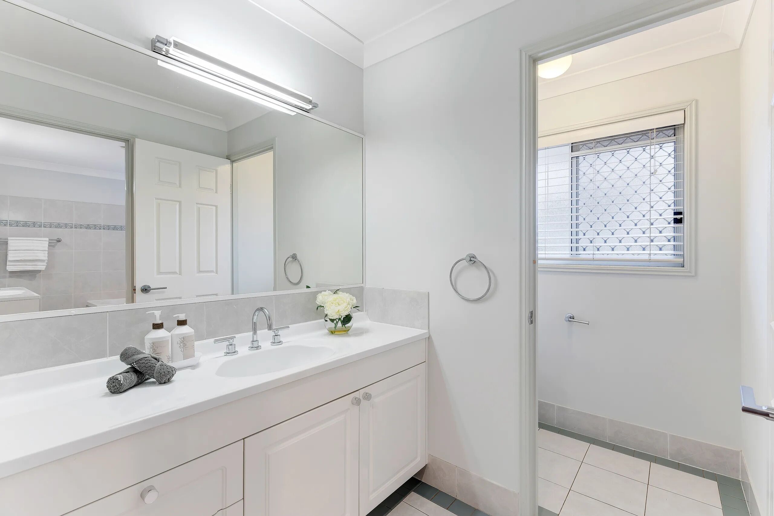 A modern bathroom with a white vanity, a large mirror, and a shower area.