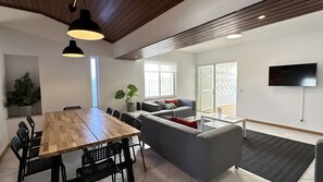 A modern living room with a wooden dining table, grey sofa, and a TV mounted on the wall. - Branca | Private Pool | 12 Pax | Albufeira (Albufeira)