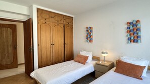Een slaapkamer met twee bedden, een garderobe, een nachtkastje met een lamp, en een muur met spoelen draad.