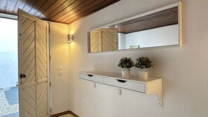 A hallway with a white console table, two potted plants, a mirror, and a wooden door. - Branca | Private Pool | 12 Pax | Albufeira (Albufeira)