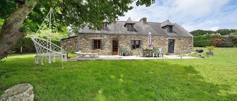 A stone house with a large lawn, a swing, and outdoor furniture.