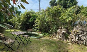 A garden with a small table and chairs, surrounded by dense foliage and a water feature.