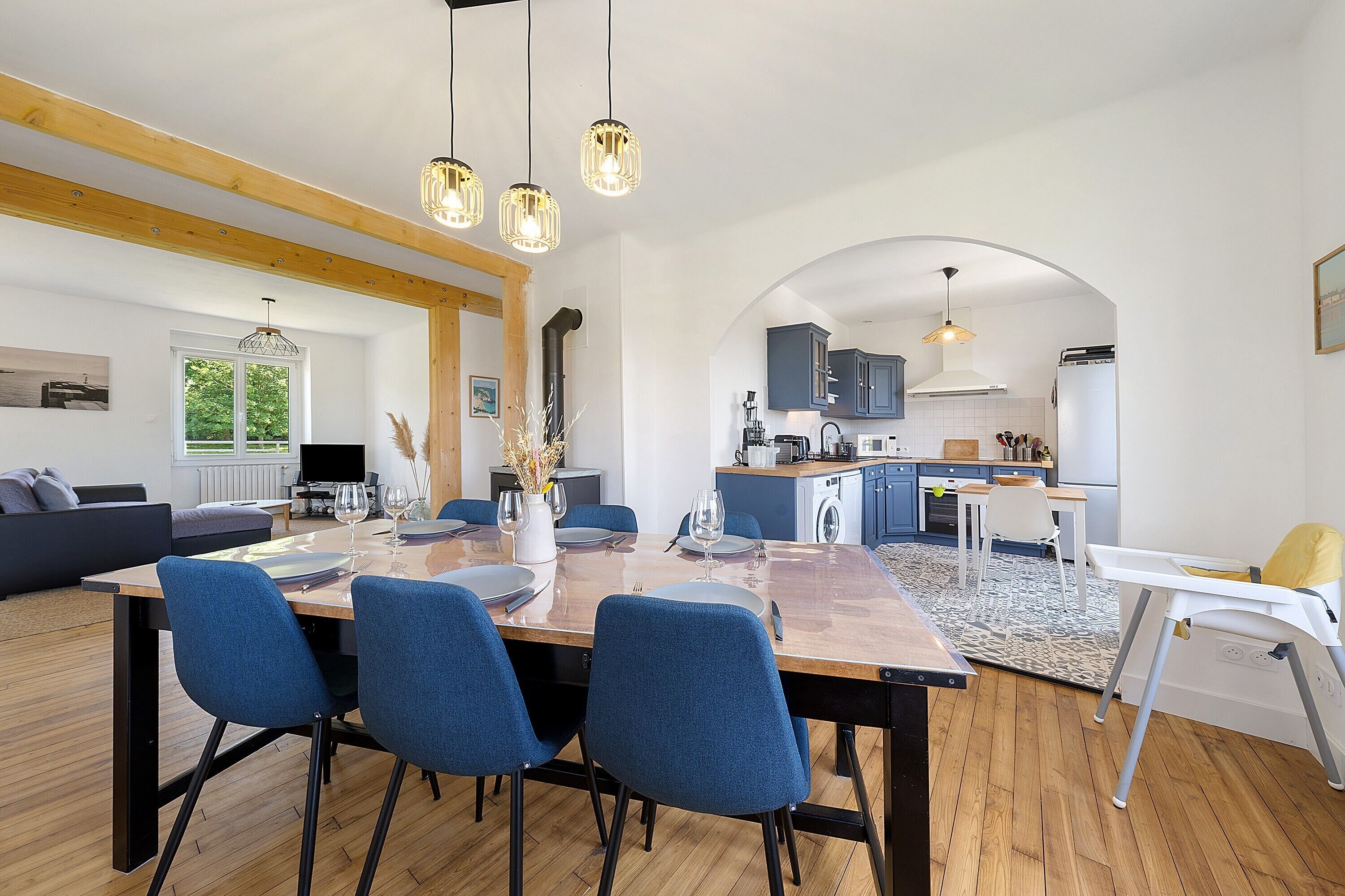 A modern kitchen with a dining area, wooden beams, and a view through an archway.