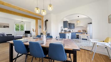 A modern kitchen with a dining area, wooden beams, and a view through an archway.