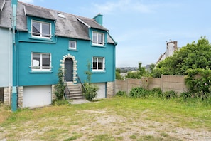 A two-story house with a stone archway entrance, a small staircase, and a view of a hill.