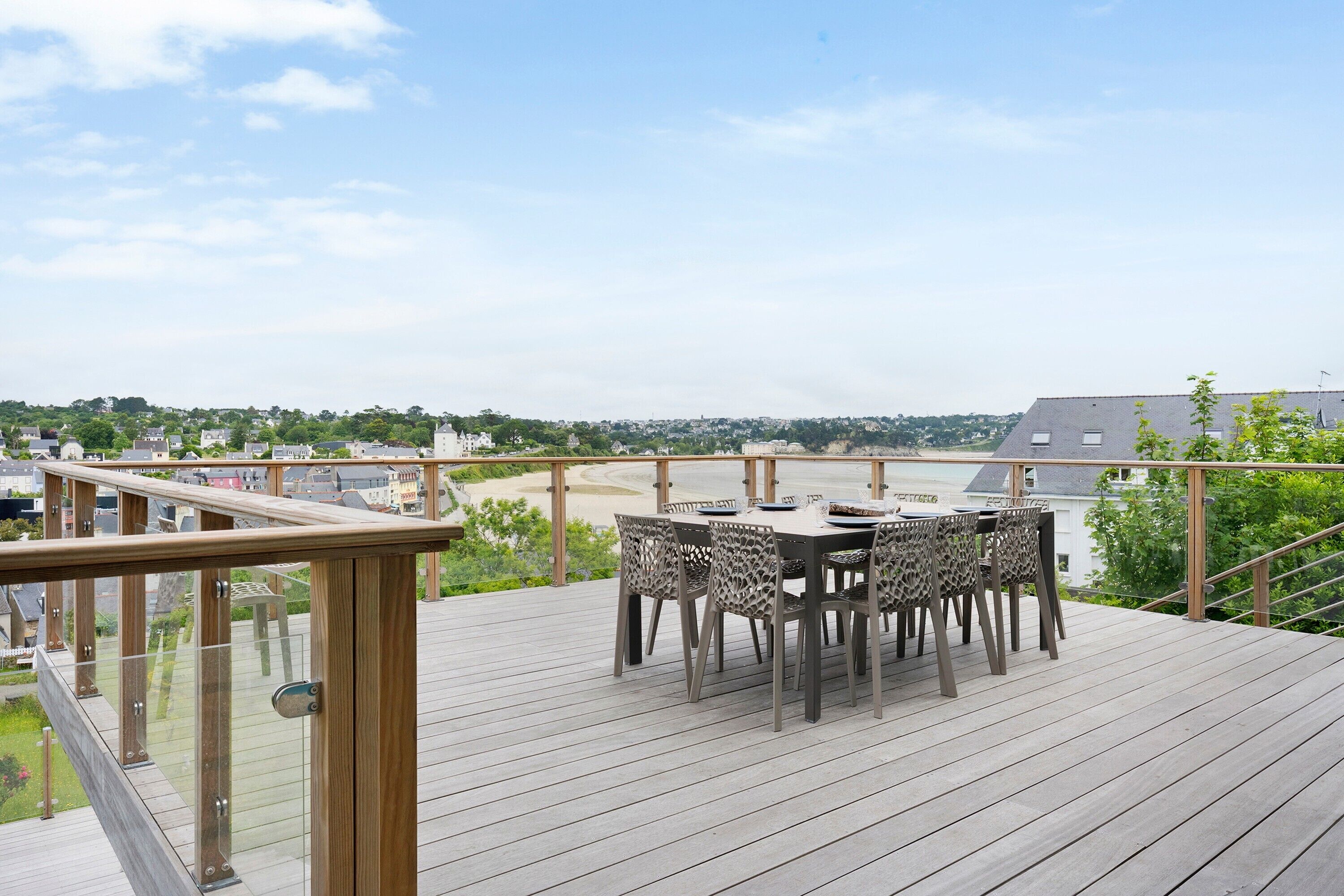 A deck with a table and chairs, overlooking a beach and buildings.