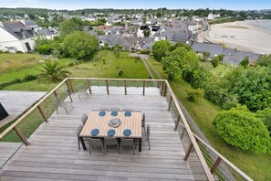 Terraza de madera con mesa y sillas, con vistas a una zona residencial y una playa.