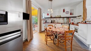 A modern kitchen with white cabinets, a dining table with chairs, a built-in oven, and a large window with curtains. - Family Home in Morgat, Enclosed Garden, 2 Minutes from the Beach (Crozon)