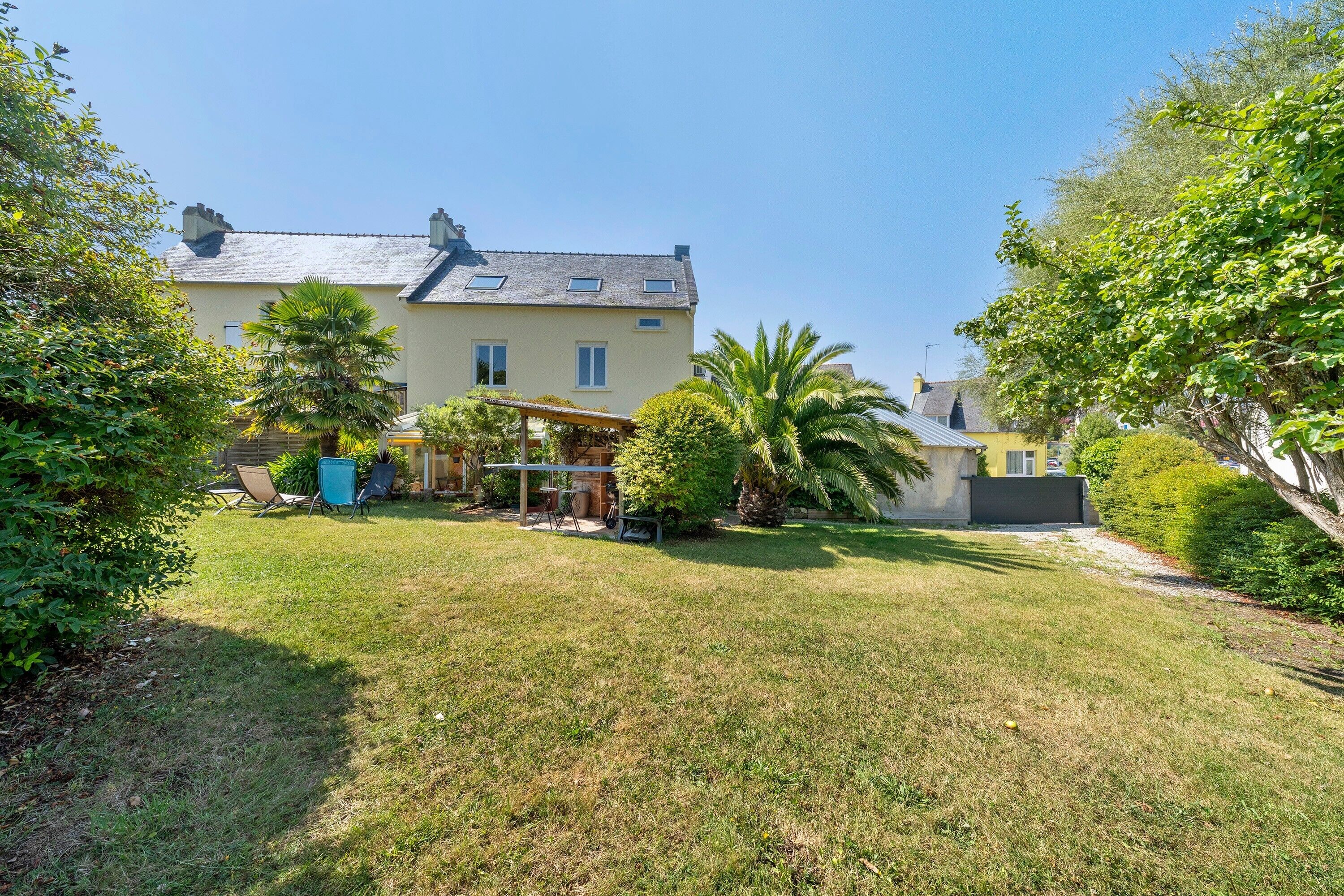 Uma casa de dois andares com varanda coberta, gramado e diversas árvores e arbustos.