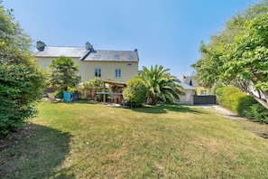 A two-story house with a covered patio, a lawn, and a variety of trees and shrubs.