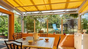 A sunlit patio with a table and chairs, a yellow awning, and a view of greenery. - Family Home in Morgat, Enclosed Garden, 2 Minutes from the Beach (Crozon)