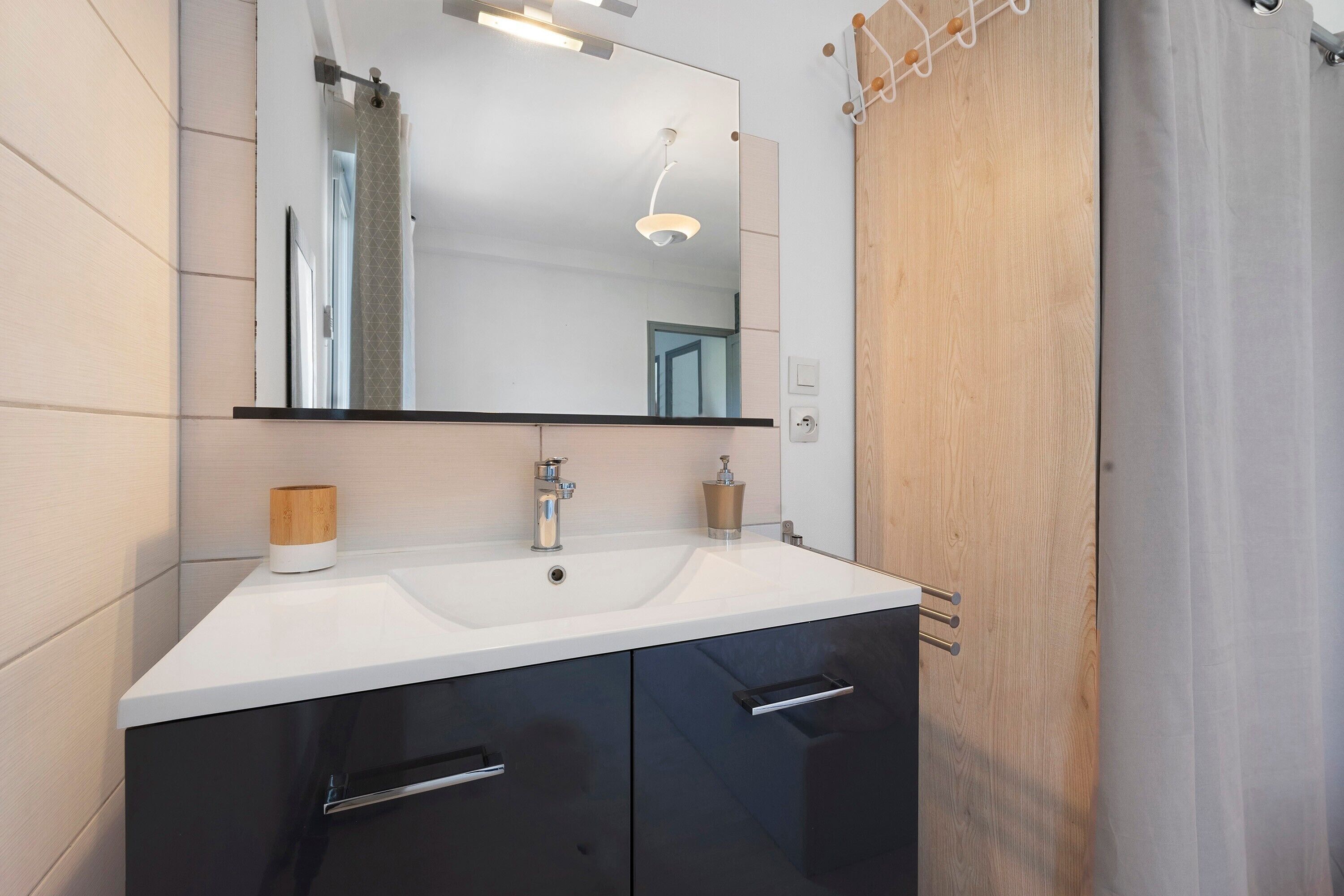 Un baño moderno con un lavamanos blanco, muebles negros y una puerta de madera.