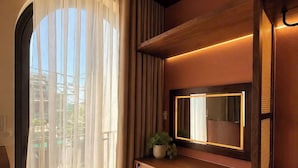 Una habitación con un escritorio de madera, un espejo, una planta en maceta y vistas a través de cortinas traslúcidas.