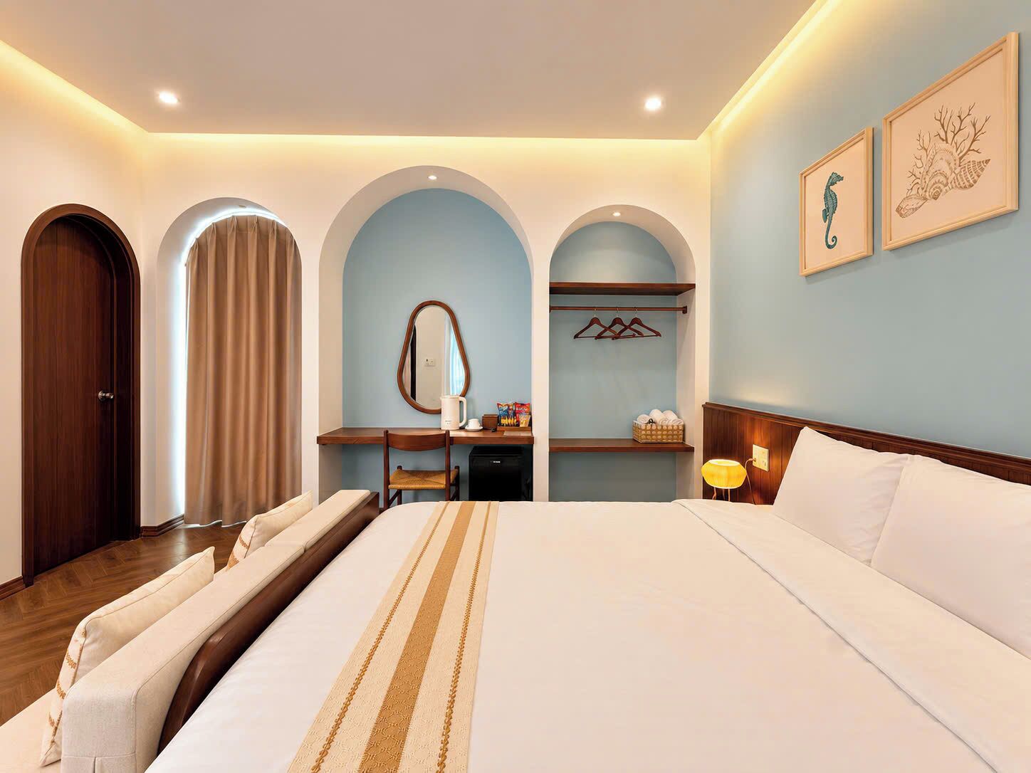 A hotel room with a large bed, a desk, a chair, a mirror, and a wardrobe.