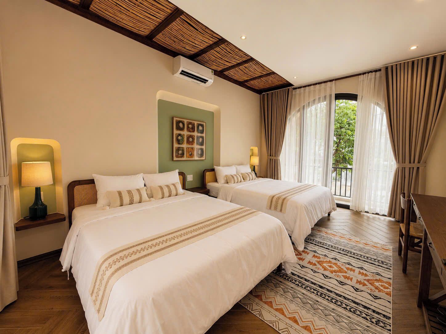 A hotel room with two beds, a large window with curtains, a ceiling fan, and a wall-mounted air conditioner.