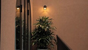 Un pasillo estrecho con una planta en maceta, un aplique de pared y una puerta de cristal.