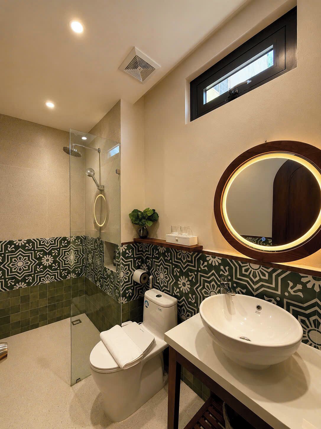 A bathroom with a glass-enclosed shower, a toilet, and a sink with a round mirror.