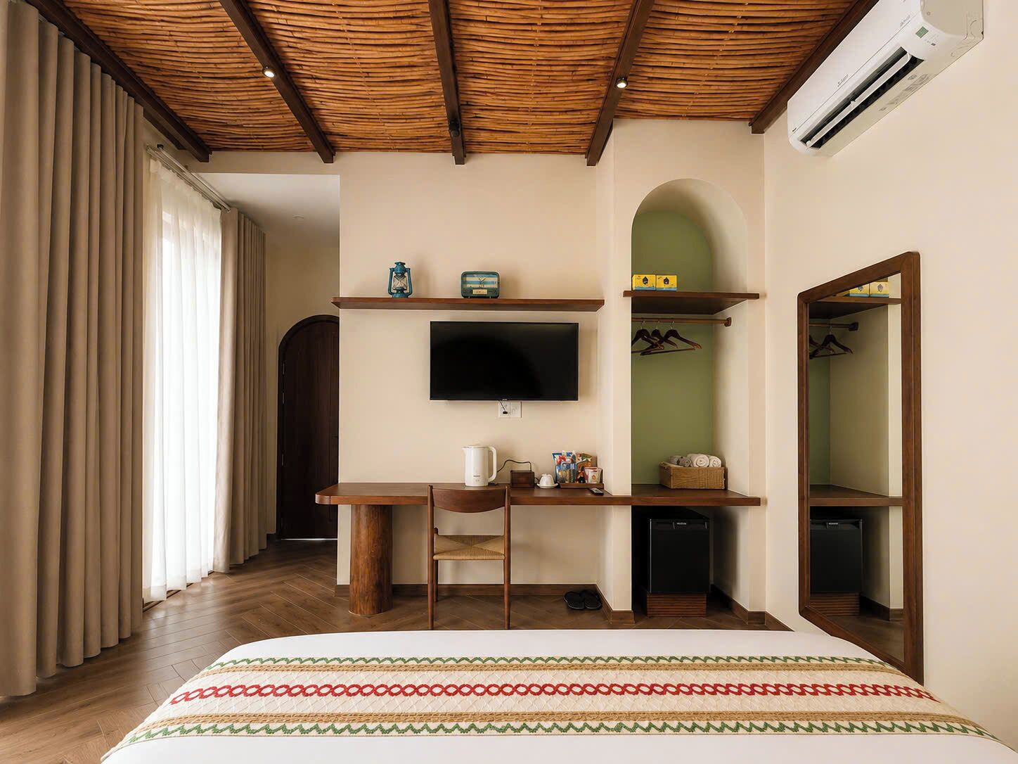 A bedroom with a bed, a desk, a chair, a television, a wardrobe, and an air conditioning unit.