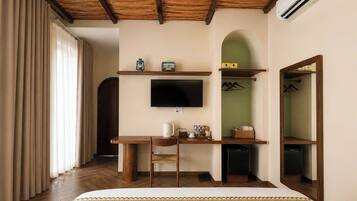 A bedroom with a bed, a desk, a chair, a television, a wardrobe, and an air conditioning unit.