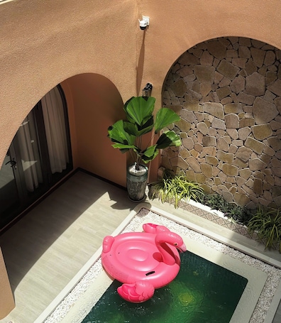 A pool area with a pink flamingo float, a potted plant, and a stone wall.. SOHO BOUTIQUE