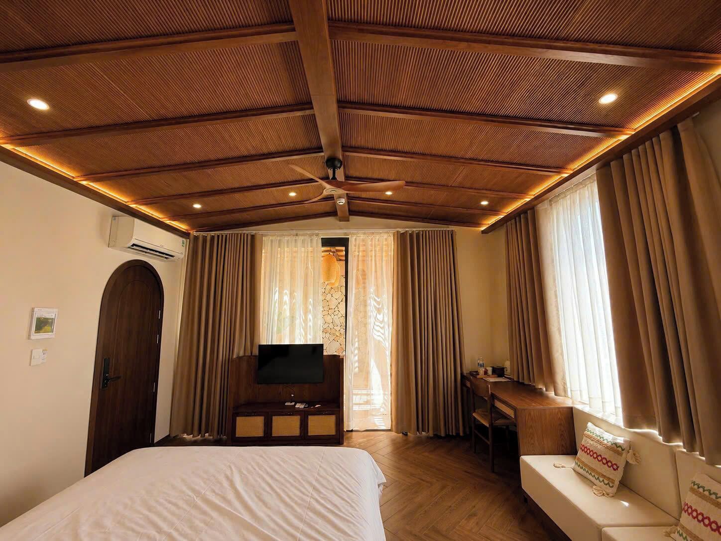 Una habitación de hotel con techo de madera, una cama, un escritorio, un televisor y cortinas.