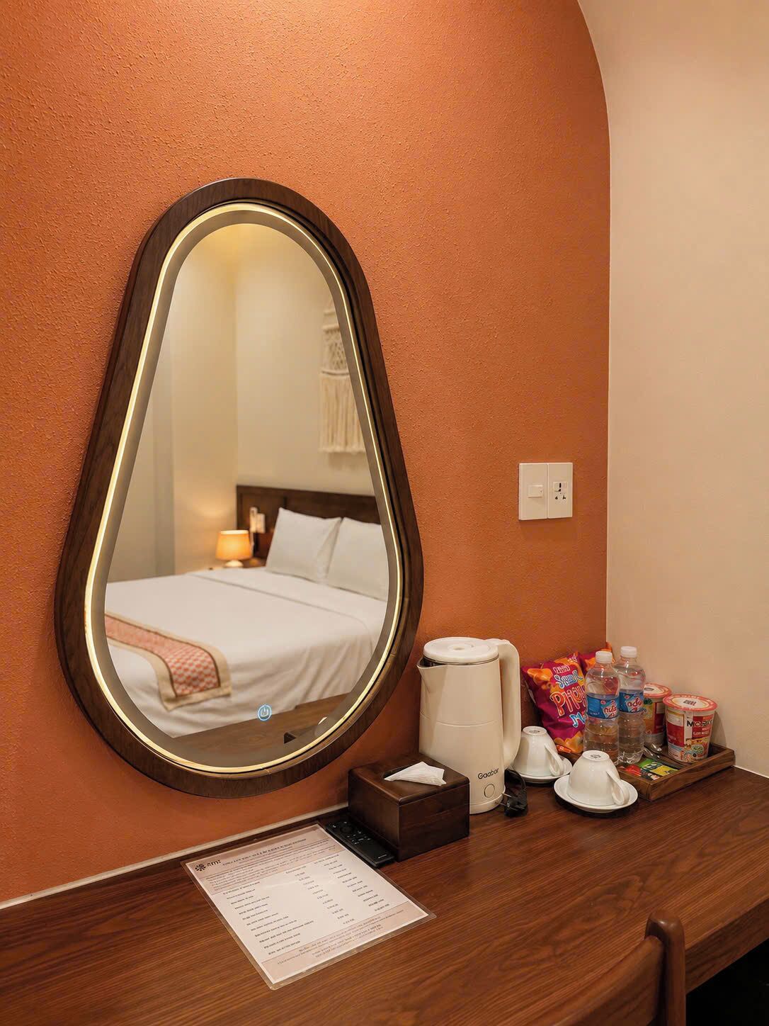 Une chambre d’hôtel comprenant un lit, une table de chevet avec une machine à café, un miroir et un plateau avec des collations et des boissons.