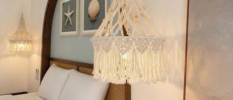 A bedroom with a bed, a macrame chandelier, a starfish decoration, and a framed picture on the wall.