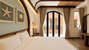 Habitación de hotel con una cama grande, una obra de arte con una estrella de mar y conchas marinas en la pared, un balcón con cortinas y un techo de madera.